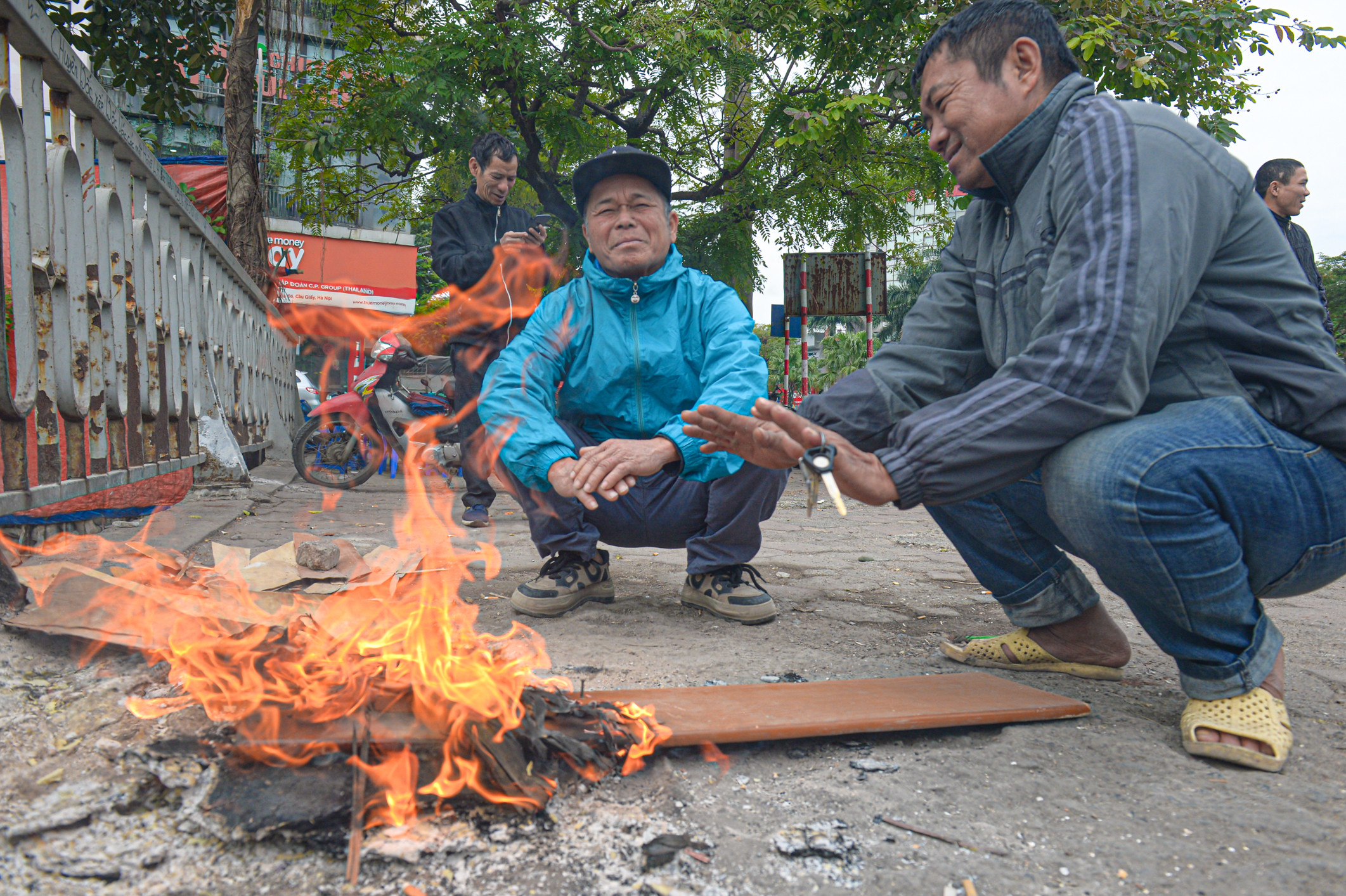 Người lao động đốt lửa sưởi ấm, mặc áo mưa tránh rét