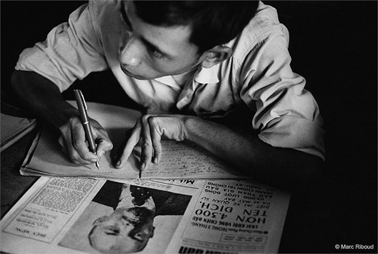 Một người đàn ông ngồi bên bàn làm việc với tờ báo Nhân Dân. 