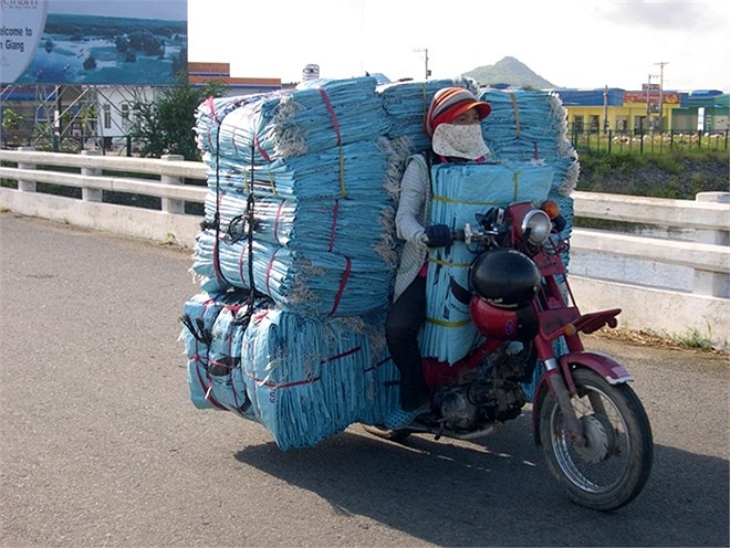 Người phụ nữ Campuchia chở những bao nylong chất đầy trên chiếc xe gắn máy và cả phía tay lái, chỉ cần sơ suất nhỏ là có thể gây ra tai nạn. 