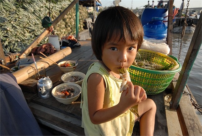Những đứa trẻ theo cha mẹ buôn bán và sống trên chợ nổi. Buổi sáng, bé ăn bánh và cháo thịt. 