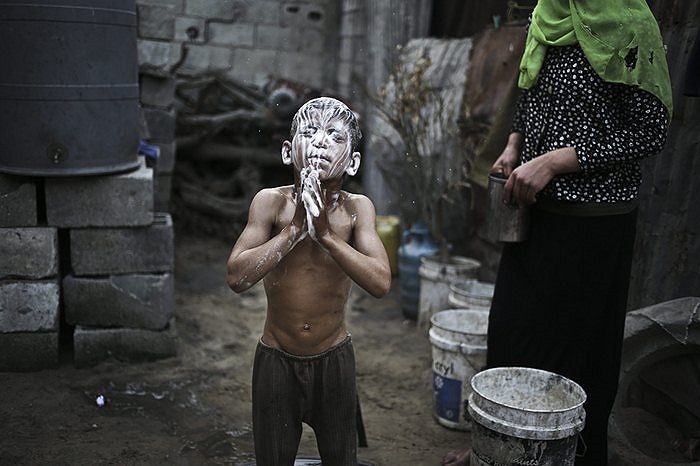 Cậu bé người Palestine đứng tắm bên ngoài khu nhà của mình tại Dải Gaza