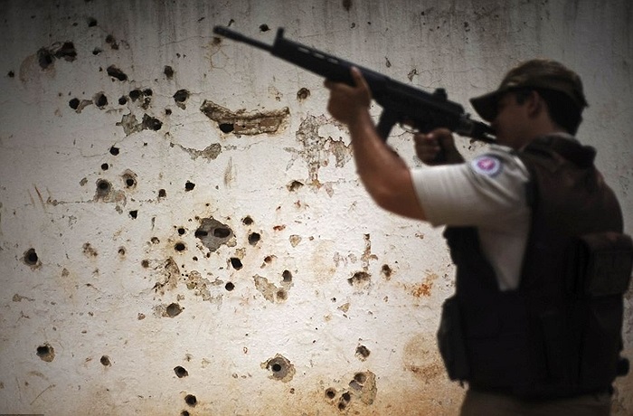 Cảnh sát tuần tra bên cạnh những vết đạn lỗ chỗ trên bức tường trắng