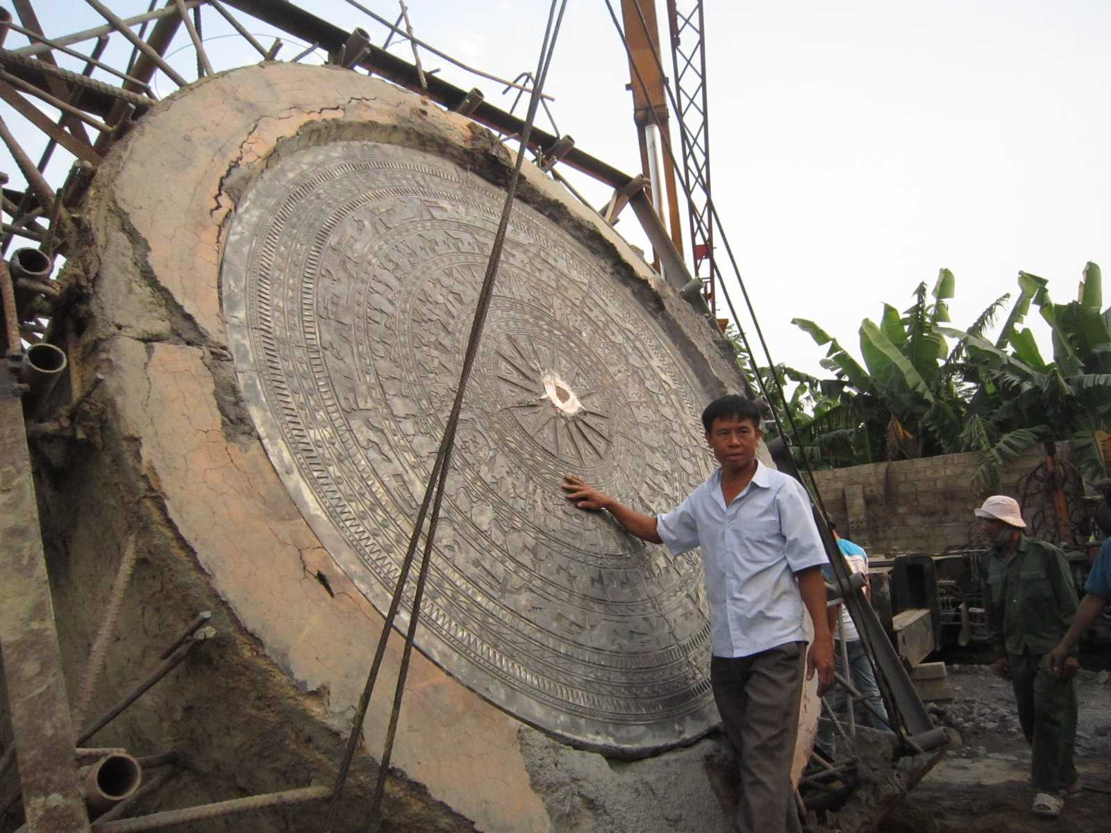 Nghệ nhân Lê Văn Bảy bên mặt trống khổng lồ đang rỡ khỏi khuôn đúc.