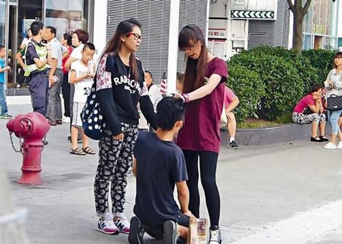 Theo những hình ảnh được cắt ra từ video, chàng trai trẻ đang quỳ xuống trước mặt 2 cô gái ở một con phố đông đúc.