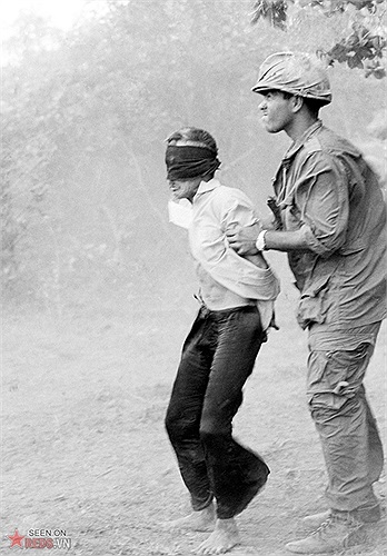 Lính Mỹ áp giải một người tình nghi là Việt Cộng giữa đám bụi mịt mù được tạo ra bởi cánh quạt trực thăng, ngày 18/4/1966