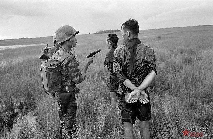 Tên lính VNCH cầm súng lục đã lên đạn khi tra vấn hai du kích nghi là Việt cộng bị bắt trong một đầm lầy đầy cỏ dại ở vùng đồng bằng phía Nam cuối tháng 8/1962