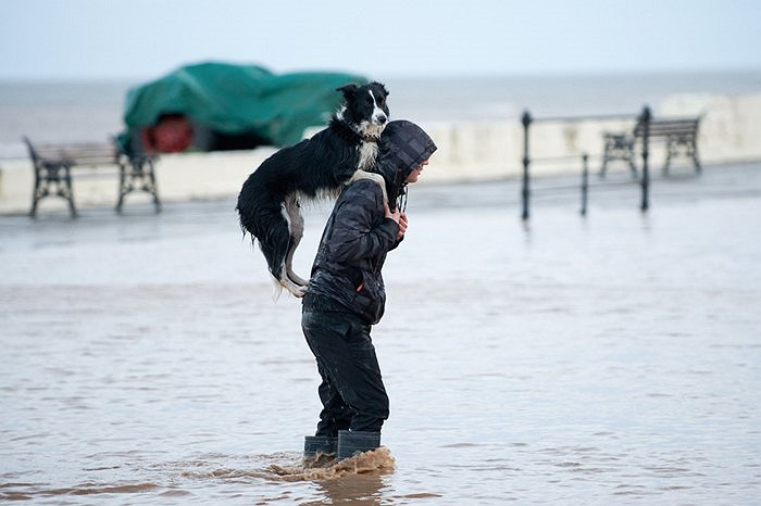 Người đàn ông và chú chó của mình di chuyển trong tình trạng ngập lụt đang diễn ra ở Saltburn, Anh