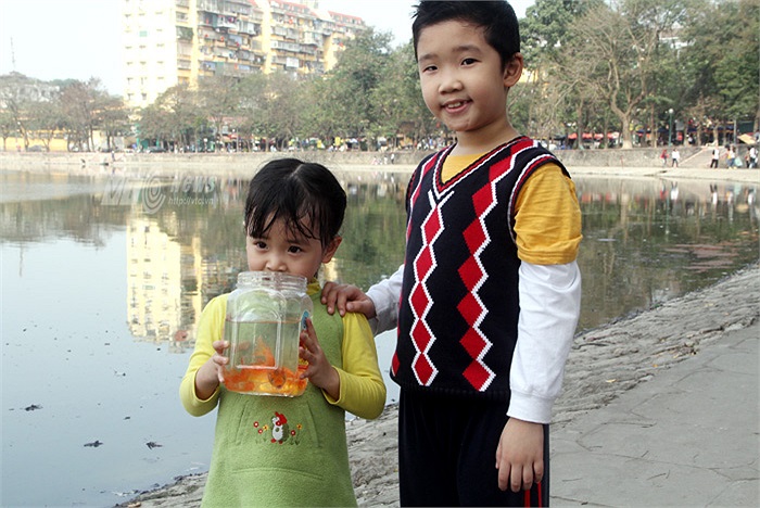 Hai em nhỏ cười tươi rạng rỡ khi được nghe các anh chị sinh viên tình nguyện giải thích về tục lệ thả cá Chép gắn với thông điệp bảo vệ môi trường