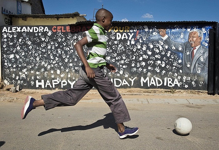 Đứa trẻ Nam Phi chơi bóng bên cạnh bức tường có dòng chữ chúc mừng sinh nhật Cựu Tổng thống Nelson Mandela