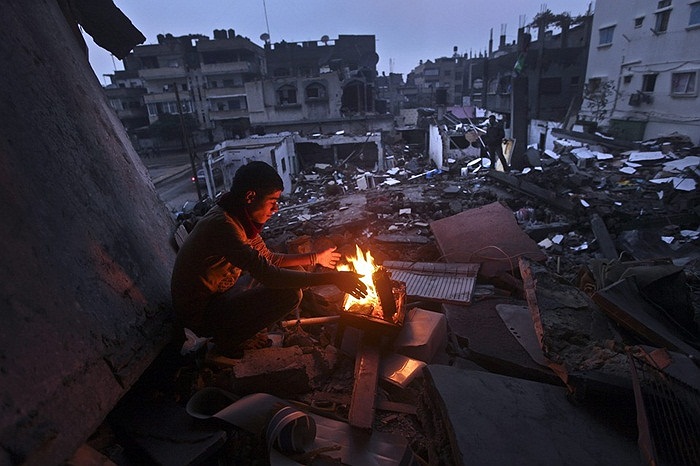 Người đàn ông Palestine ngồi sưởi ấm trên đống đổ nát từng là nhà của mình ở dải Gaza