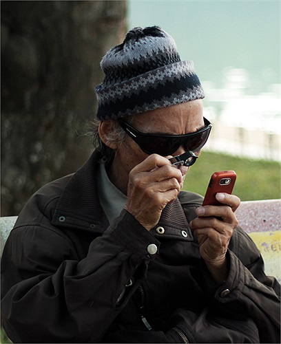 Một ông cụ dùng kíp lúp để xem điện thoại bên bờ Hồ Gươm.