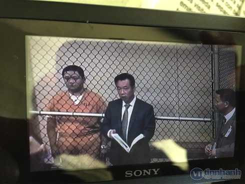 Minh Béo đứng sau lưới thép để nghe luận tội.