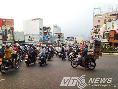 Chiếc xe máy chở hàng cồng kềnh chen vào dòng xe cộ đông đúc để băng qua đường 