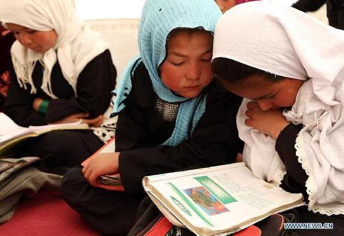 Hai bé gái nhỏ nhắn đang chăm chú đọc sách theo sự hướng dẫn của giáo viên.