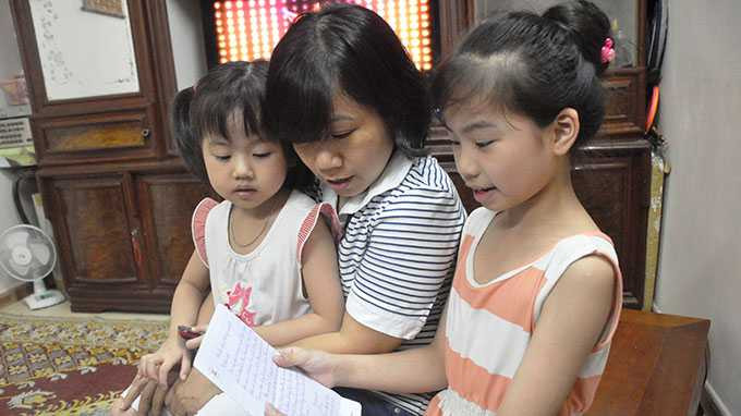 Chị Vũ Thị Bích Thuận cùng bé Minh Châu (bìa phải) và Hương Giang xem lại bức thư trước khi gửi cho đại úy Phạm Đức Hạnh - Ảnh: Quang Thế/TTO