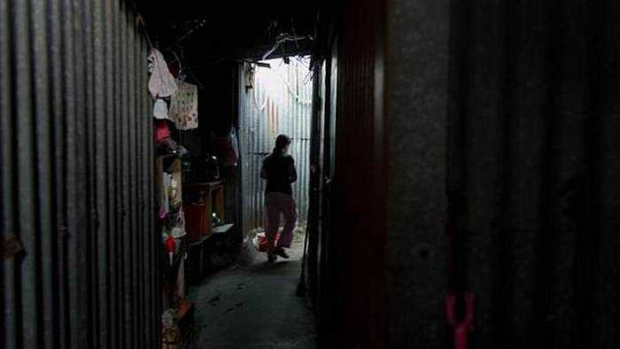 Một cư dân đi giữa con đường mà xung quanh là các bức tường dựng bằng tôn