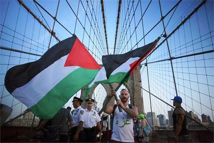 Một người đàn ông giữ hai lá cờ trong cuộc biểu tình ủng hộ Palestine đi qua cầu Brooklyn ở Manhattan, New York