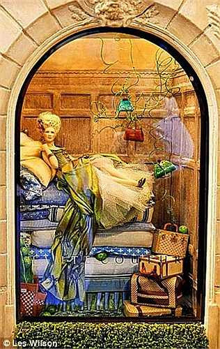 Và đây là một người mẫu, diện bộ đầm diêm dúa, tạo dáng bên trên chồng đệm và túi xách, va li của một cửa tiệm khác. Tất cả các mẫu vải dùng trong nhà búp bê đều được sơn thủ công. 