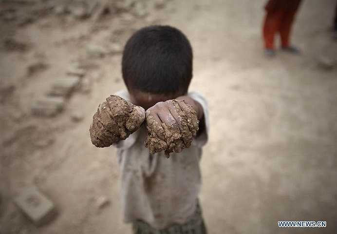 Hình ảnh một lao động nhí giơ bàn tay lấm lem bùn đất trong giờ làm việc tại xưởng gạch.