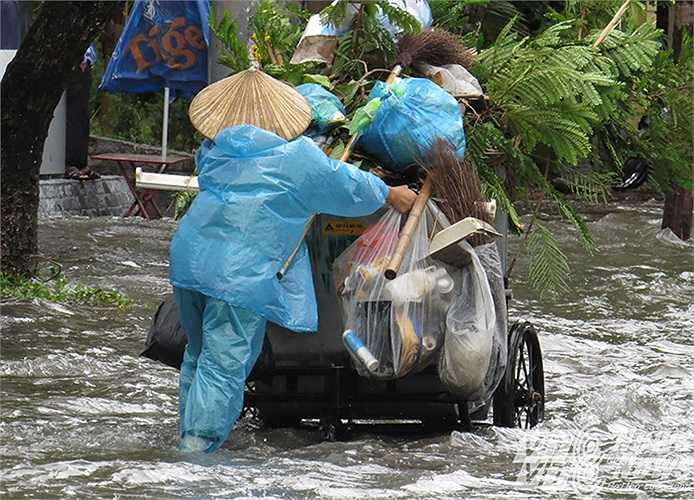 Nữ công nhân môi trường nhọc nhằn đẩy chiếc xe rác trên đường phố ngập nước