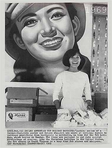 SAIGON 13/2/1969 - NHỮNG NỤ CƯỜI MỜI CHÀO MUA MÓN HỜI DỊP LỄ TẾT--Những nụ cười rạng rỡ của cô gái trong bức tranh cổ động lớn hơn kích thước thật, và của cô gái bán hàng tại Saigon nhằm lôi kéo khách hàng mua tất cả mọi thứ từ kem đánh răng (Hynos) đến những viên long não, đúng vào thời điểm những ngày nghỉ Tết, bắt đầu vào hôm thứ hai. 