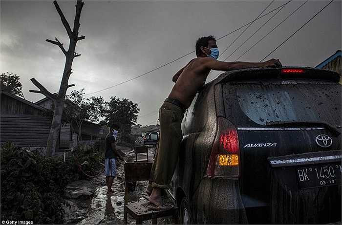 Người đàn ông rửa xe ô tô bị khói bụi núi lửa bám vào