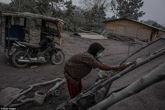 Người phụ nữ gạt bụi khỏi mái bạt trên căn lều của mình