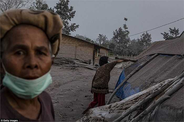 Người phụ nữ gạt bụi khỏi mái bạt trên căn lều của mình