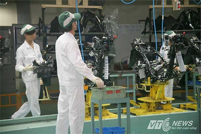 Động cơ, dây điện được gắn lên trước tiên. Kế đến là các chi tiết nhựa, bình xăng...Kỹ thuật viên của Honda đứng 2 bên và lắp ráp mọi thứ vào chiếc xe