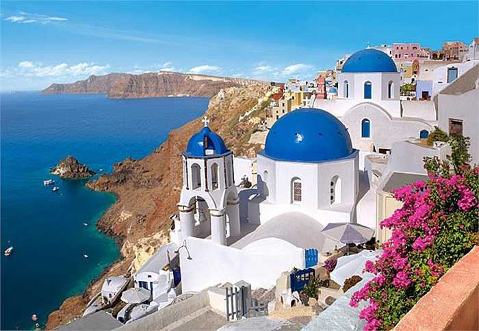 Santorini, Hi Lạp nổi tiếng với những vách đá dựng đứng ôm lấy bờ biển cát đen đặc trưng của bụi núi lửa, cùng với nét kiến trúc độc đáo của hai gam màu trắng và xanh da trời.