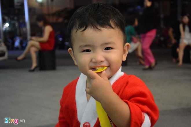 Ông già Noel nhí ngậm cả đai quần áo vui chơi trước sảnh tòa nhà Bitexco, quận 1.