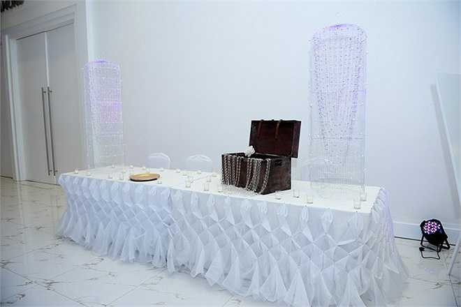 Tiệc cưới của Lê Thúy và Khải An có tông màu trắng - vàng chủ đạo. Bàn đón khách được bao phủ bởi những vật dụng trang trí tông trắng trong trẻo, cách bày trí khá đơn giản với điểm nhấn là chiếc thùng gỗ mộc mạc được đặt ngay ngắn trên mặt bàn. 