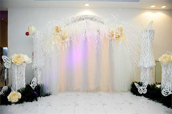 Cổng hoa của lễ cưới cũng sử dụng gam màu trắng vàng nhã nhặn. Nổi bật giữa các vật dụng trang trí gam trắng là những bông hoa hồng giấy cỡ lớn, tông màu vàng trang nhã. Theo chú rể, tông màu trắng vàng toát lên vẻ sang trọng, lịch thiệp cần thiết và cũng là gam màu yêu thích của cô dâu.