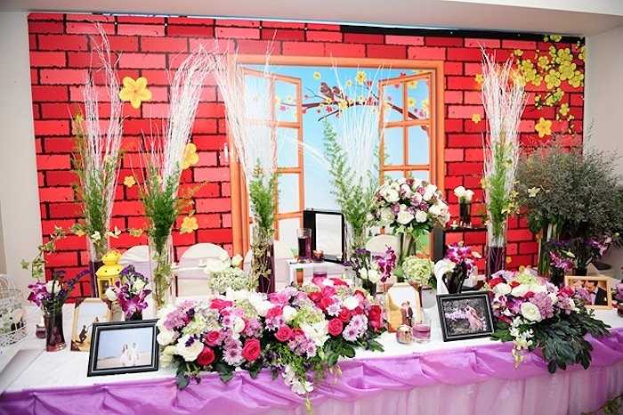 Bàn trang trí ở sảnh tiệc được thiết kế bắt mắt với những lẵng hoa hồng lãng mạn, lồng ghép là ảnh cưới của đôi vợ chồng trẻ được chụp ở nhiều địa điểm đẹp phía Nam. 