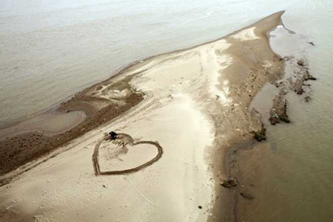 Nhiệt độ lạnh dưới 10 độ C, Tuấn Anh (Hà Nội) vẫn hì hục đào, vẽ trên nền cát giữa mặt sông Hồng trái tim lớn viết tên 2 người để tặng bạn gái. 