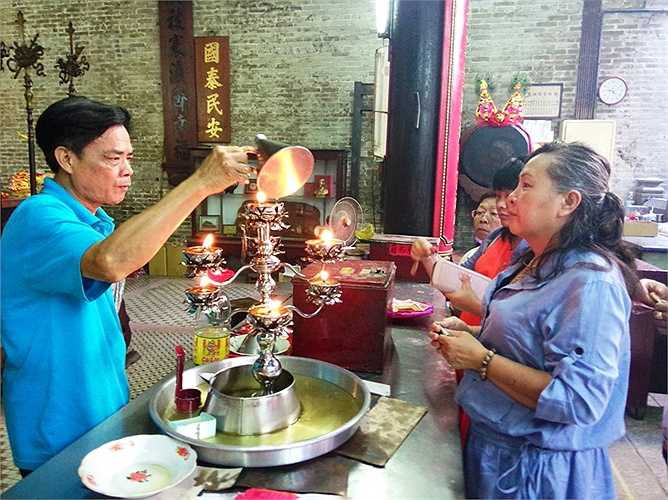 Đọc họ tên người muốn được cầu an, tưới dầu lên nến đang cháy chứng giám lời cầu nguyện. (Ảnh: Phan Cường)