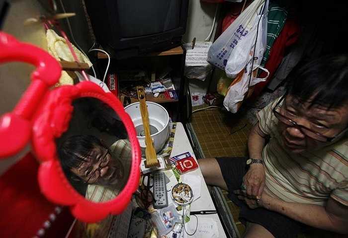 Toàn bộ căn nhà 55 m2 được chia thành 19 phòng cho thuê. Ảnh chụp người đàn ông ngồi trong phòng rộng 2m2 đặt vừa chiếc giường ngủ