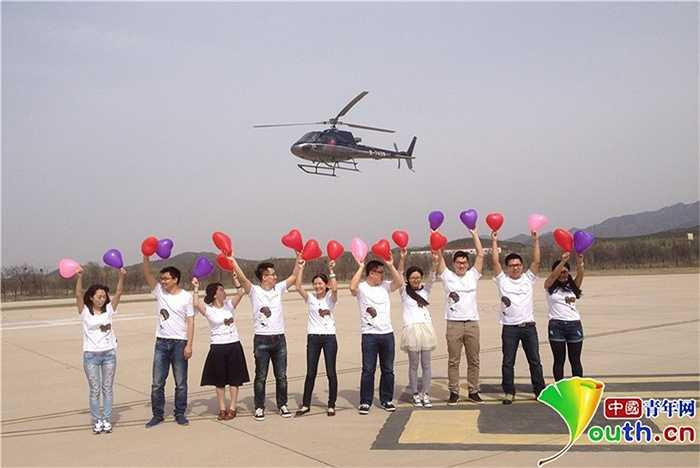 Trong khi máy bay trên trời, bạn bè của chàng trai đứng dưới cầm bóng bay trái tim và mặc áo có hình chữ 'marry' - cưới hò reo