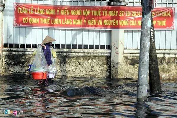 Trên đường Kinh Dương Vương, nước ngập đoạn dài khoảng 1 km. Trong ảnh: Chị Nguyễn Thị Lài (40 tuổi, quê Bình Định) bì bõm men theo vỉa hè về nhà sau khi bán hết gánh hàng rong.