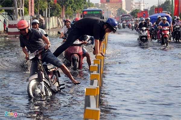 Nước ngập khiến xe chết máy, thanh niên trèo lên dải phân cách để tránh bị ướt.