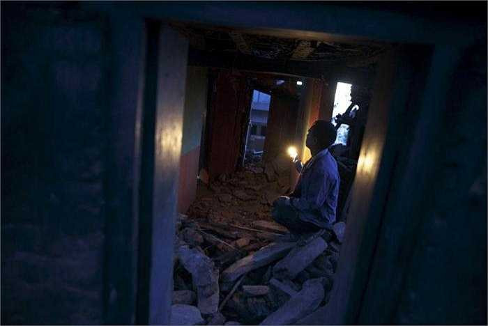 Một người đàn ông đang dùng đèn để tìm lại những vật dụng còn có thể dùng được trong căn nhà đổ nát sau trận động đất kinh hoàng (Minh Chiến/ Theo Reuters)