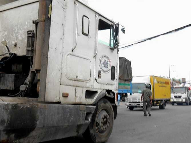 Một bảo vệ dân phố lọt thỏm trước các xe container, xe tải khi xuống đường điều tiết giao thông.