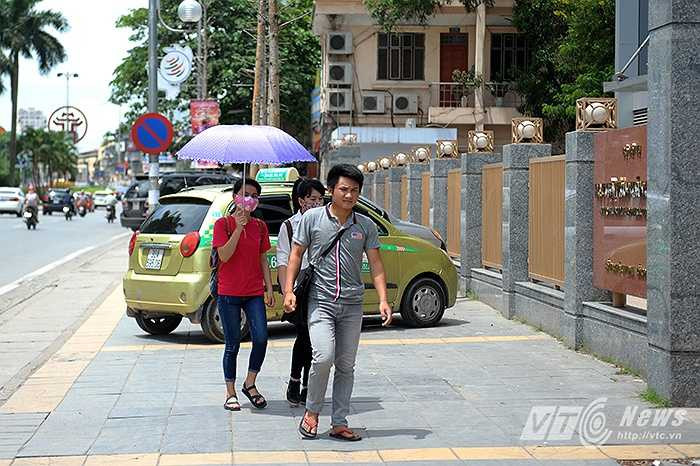 Người đi đường trong cái nắng gay gắt dưới hàng cây mỡ không lá đoạn qua trước cổng Học viện Hành chính Quốc gia.