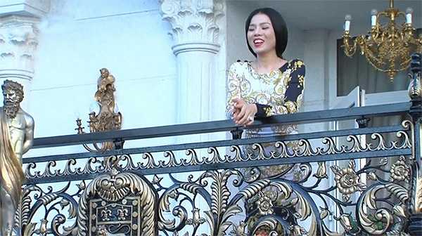 Ca sĩ Lệ Quyên, người cố vấn cho đội của Đàm Vĩnh Hưng, đứng trên ban công trước cửa nhà. Lan can chạm trổ cầu kỳ với nhiều hình ảnh mang lại may mắn cho gia chủ.