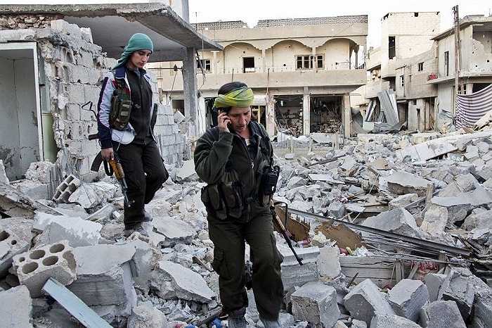 Các nữ binh sĩ người Kurd đi qua đống đổ nát ở khu vực đang tranh chấp Kobani, Syria