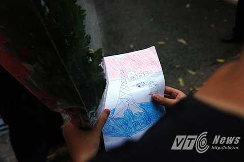 Một bé gái mang theo bức tranh vẽ cờ Pháp, tháp Eiffel và dòng chữ: ‘Chúng tôi yêu Pasis’