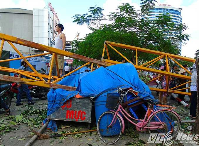Thân cần cầu đổ đập xuống qua hàng rào sắt bảo vệ công trường, đè vào đống đồ đạc, hàng hóa của người dân để bên lề đường.