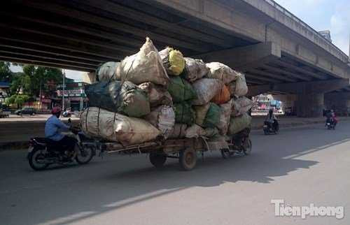 Một chiếc xe máy kéo theo đằng sau là chiếc xe bò chở hàng chục bao phế liệu đi trên đường Nghiêm Xuân Yêm đoạn ngã ba Nghiêm Xuân Yêm - Kim Giang (Hoàng Mai, Hà Nội).