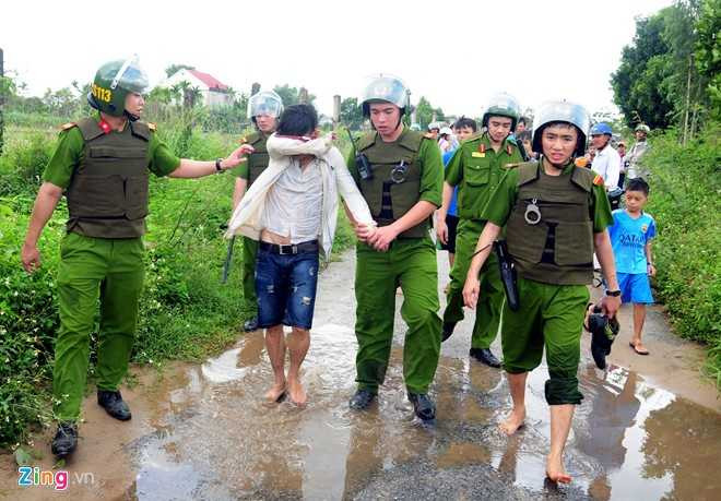 Thanh niên ướt sũng, lấy tay che mặt khi bị cảnh sát dẫn giải đi. 