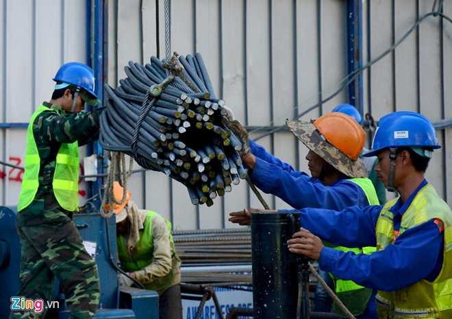 Trên mặt sàn công trường, sau khi cắt uốn các thanh thép, nhóm công nhân phối hợp nhịp nhàng đưa thép xuống hầm từ các lỗ mở.